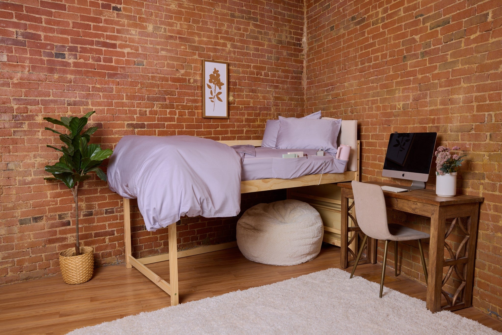 Room with a loft bed, desk, and decor against a brick wall.