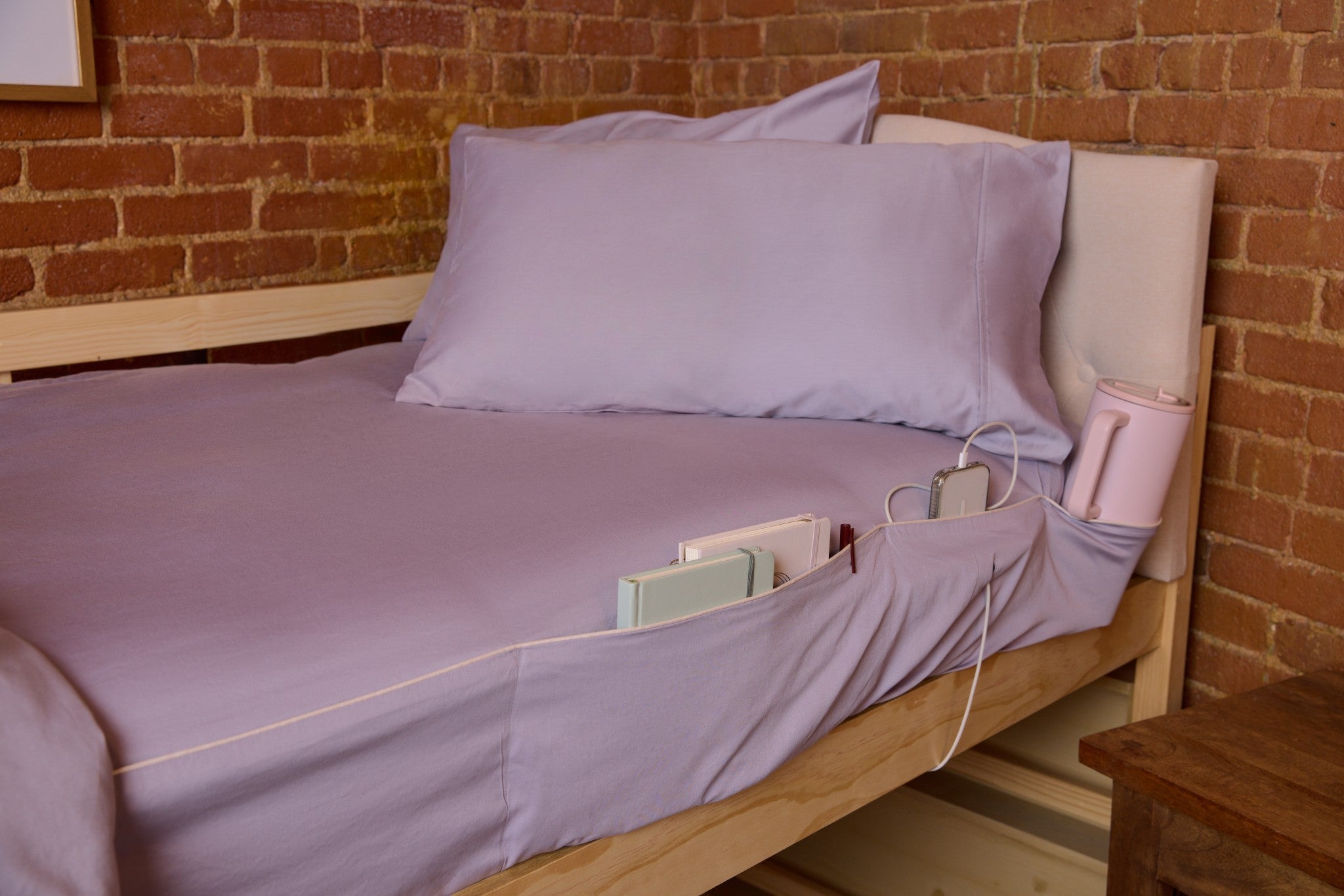 Bed with purple bedding and pillows against a brick wall.