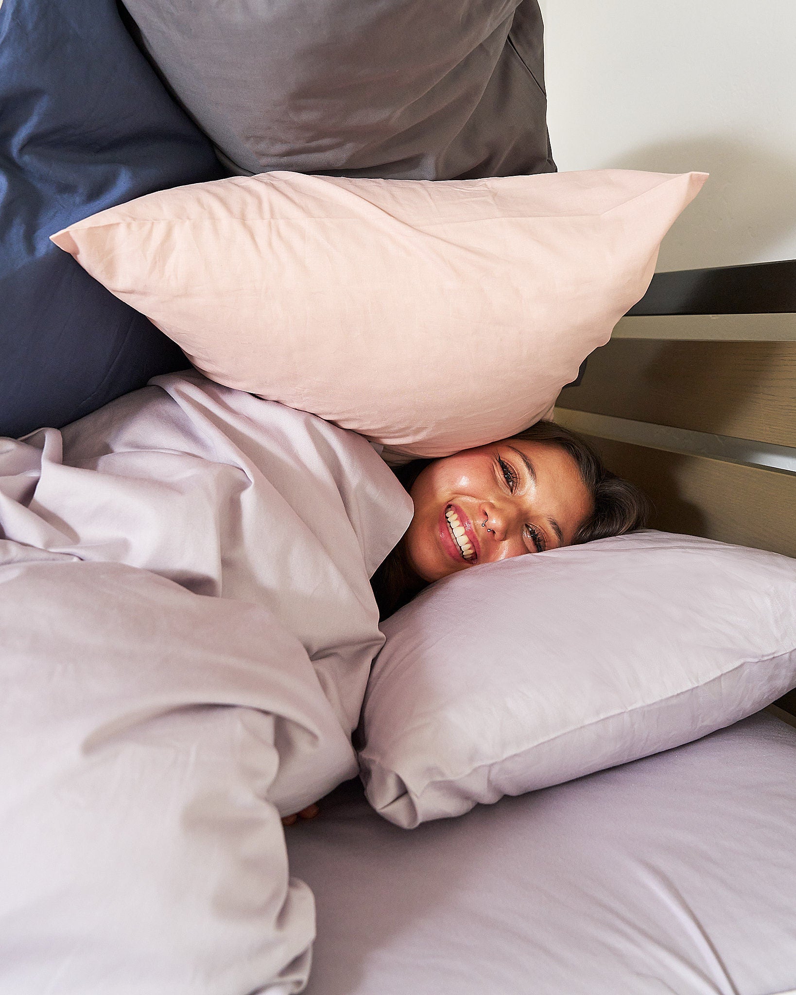 Twin XL Duvet and Pillowcases. Dorm Student laughing in bed on a lavender purple fitted sheet with side storage, wrapped in a l100% Cotton, 400 thread count avender purple duvet and her face in between fluffy pillows